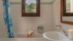 Une salle de bain avec une baignoire, un lavabo, une fenêtre et un miroir.