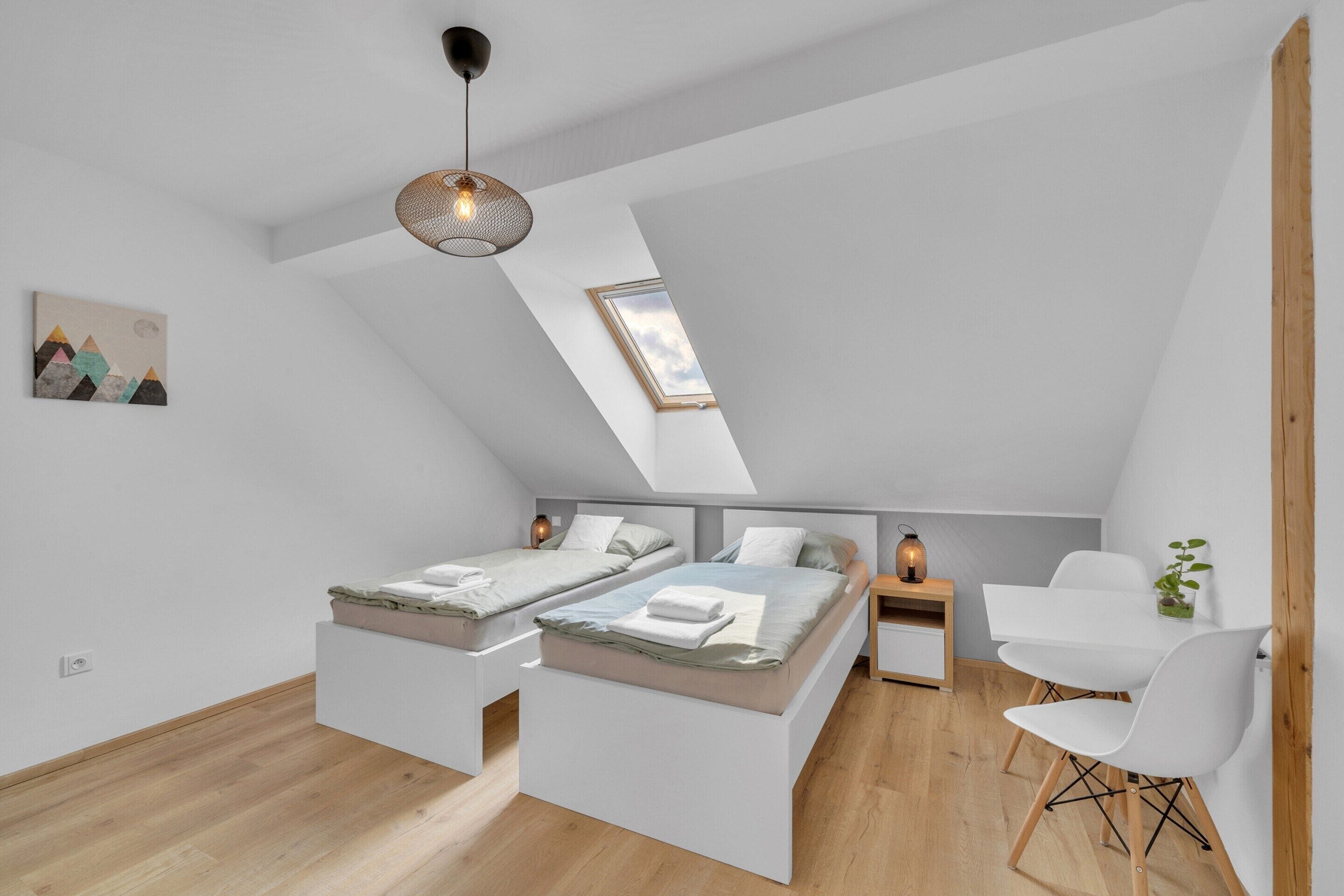 A modern loft bedroom with a skylight, two beds, a desk, and a chair.