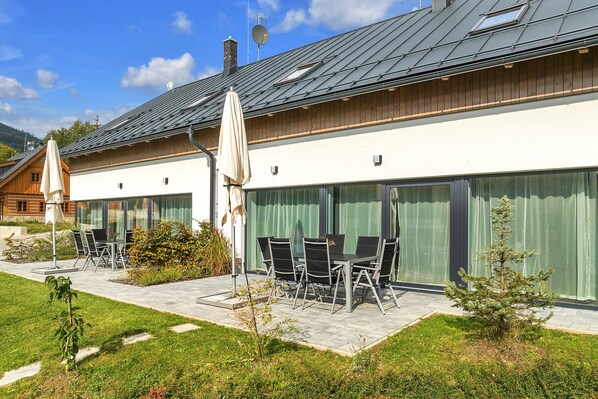 A modern house with a patio area featuring outdoor furniture and a small tree. - Villa in Krkonose With Sauna and Forest Views (Cerny Dul)