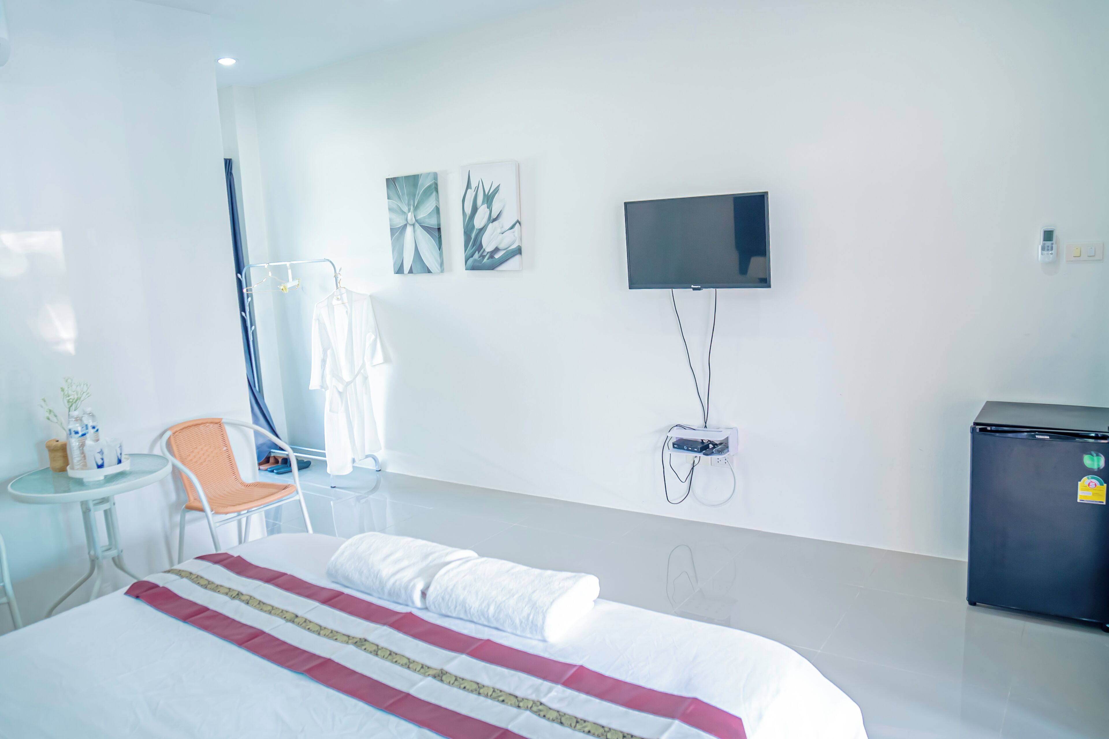 A hotel room with a bed, a TV mounted on the wall, a small table with a chair, and a refrigerator.