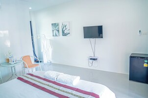 Habitación de hotel con cama, televisor montado en la pared, una pequeña mesa con una silla y un refrigerador.