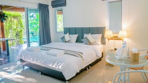 A modern hotel room with a large bed, a glass table with chairs, a balcony, and a view of greenery. - Farinda Resort & Pool Villa (Chom Thong)