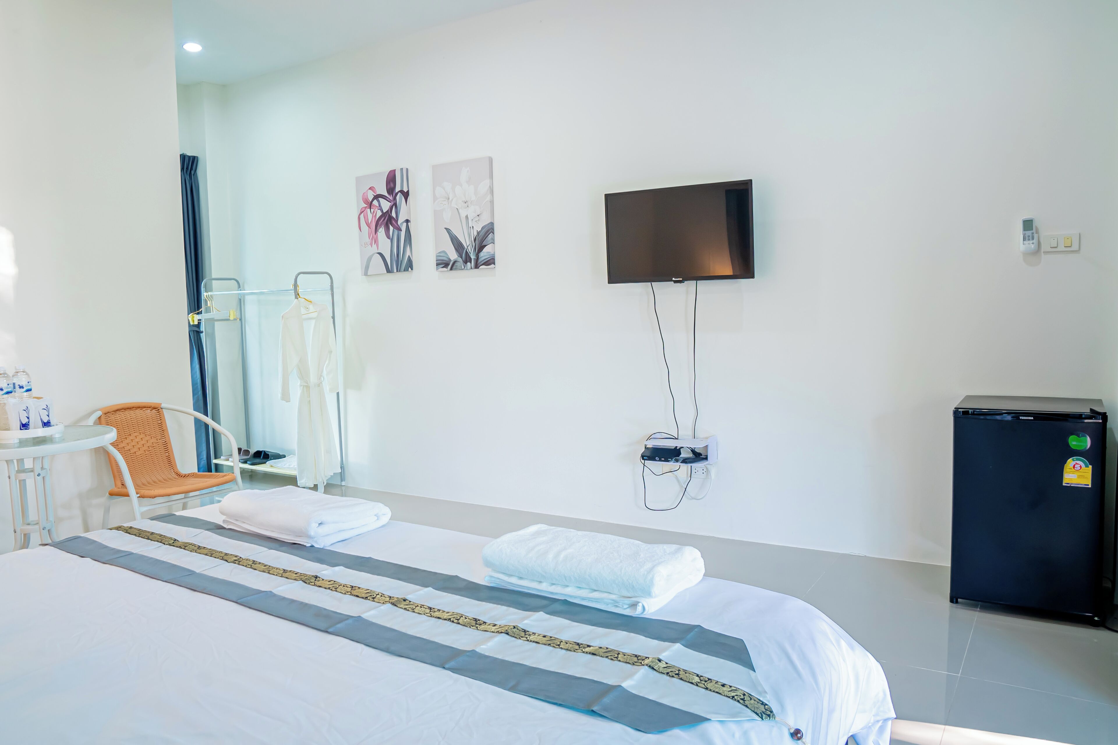 A hotel room with a bed, a TV mounted on the wall, a small refrigerator, and a chair.