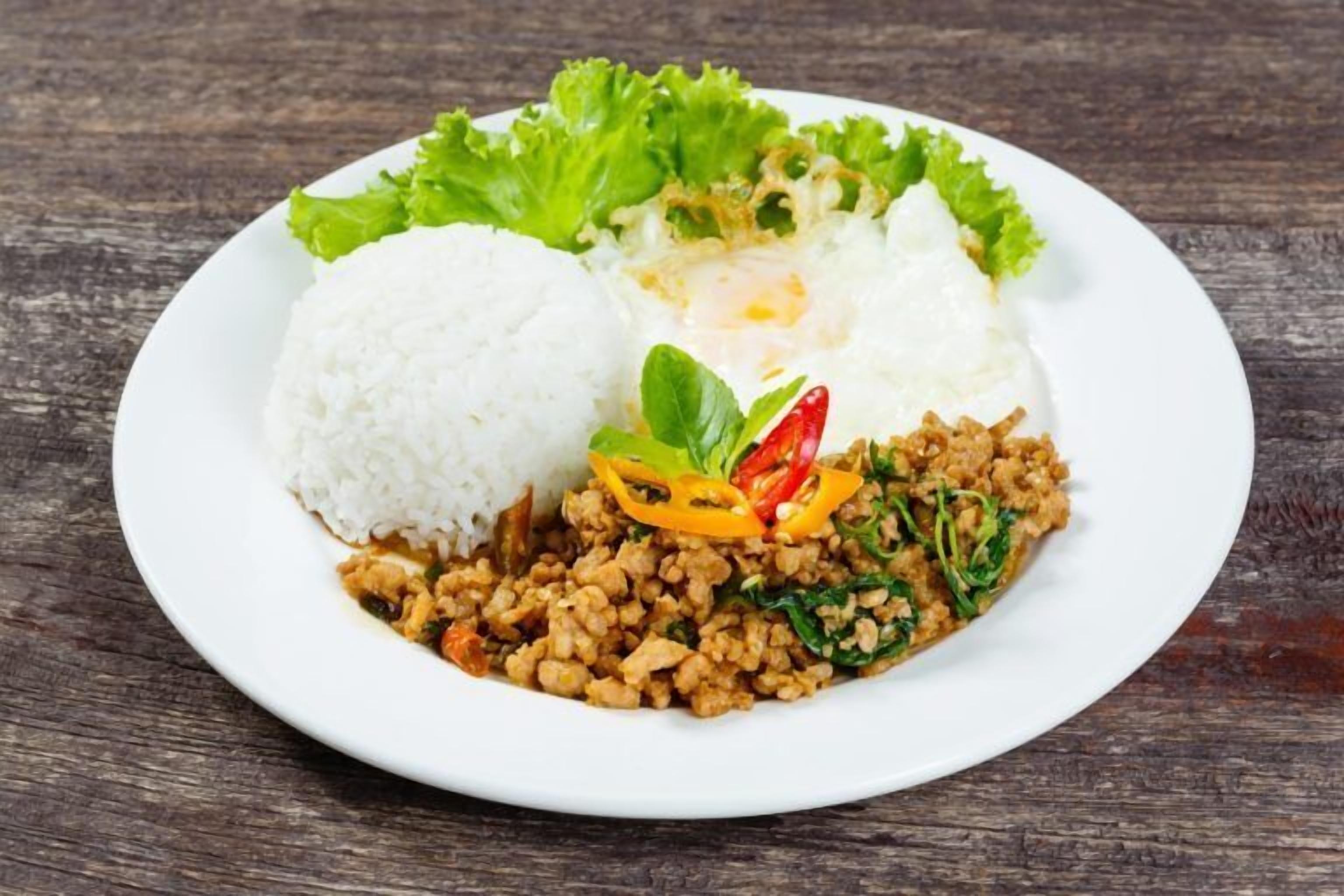 Un plato de comida con arroz, un huevo frito y un salteado de verduras, presentado en un plato blanco.
