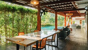 An outdoor dining area with a wooden table and chairs, surrounded by a bamboo fence and a view of a swimming pool. - Farinda Resort & Pool Villa (Chom Thong)