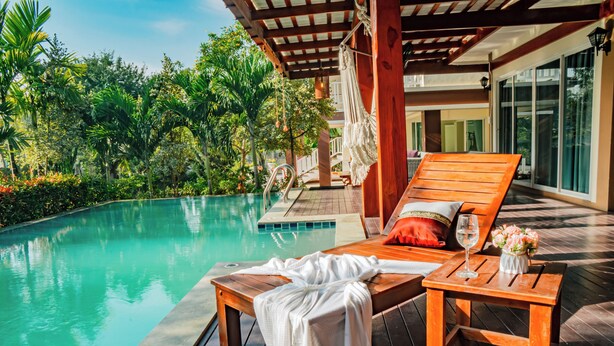 A wooden deck with a pool, lounge chairs, and a table with a glass of wine and flowers. - Farinda Resort & Pool Villa (Chom Thong)
