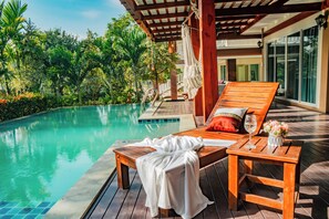Eine Holzterrasse mit Pool, Liegestühlen und einem Tisch mit einem Weinglas und Blumen.