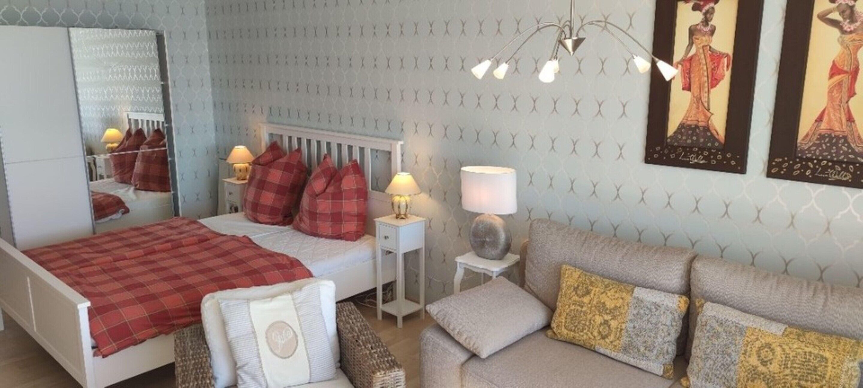 A bedroom with a bed, a nightstand, a lamp, a sofa, and a mirror.