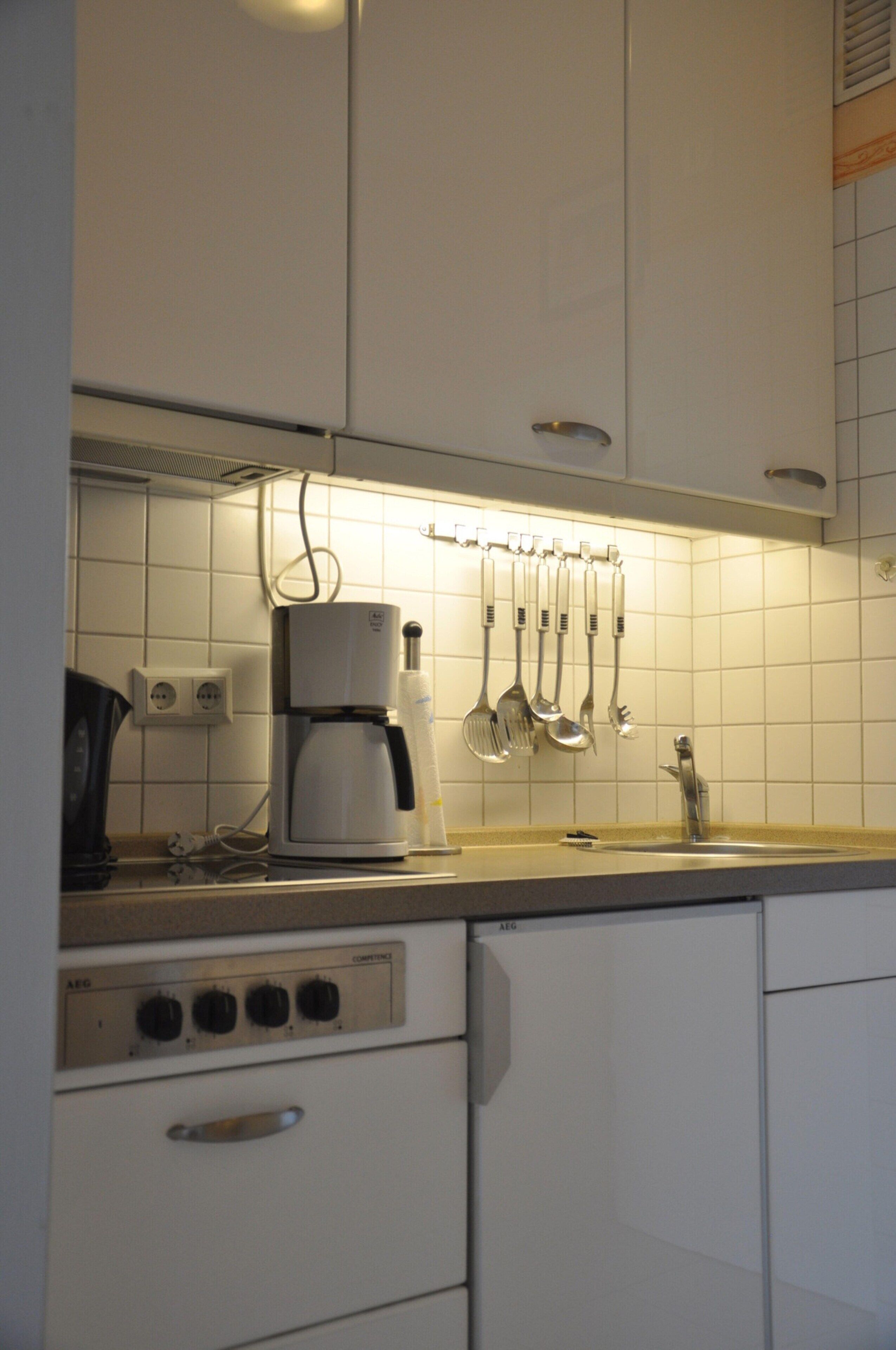 A kitchen with white cabinets, a coffee maker, and utensils hanging on the wall.