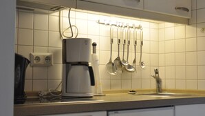 A kitchen with white cabinets, a coffee maker, and utensils hanging on the wall. - Holiday Home in Fehmarn by the Beach (Fehmarn)
