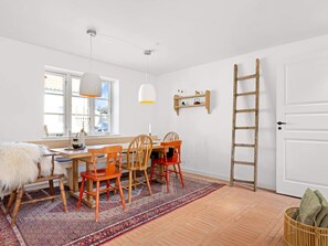 A room with a wooden desk, chairs, a hanging light fixture, a ladder, and a window with a view.