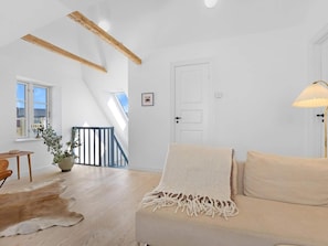 A modern living room with a sloped ceiling, a sofa with a throw blanket, a wooden floor, and a potted plant. - 5 Star Holiday Home in Lokken (Lokken)