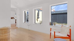 A spacious room with large windows, a wicker basket, and a modern chair. - 5 Star Holiday Home in Lokken (Lokken)