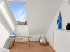 A small, bright room with a skylight, a wooden bench, a wicker basket, and a white cabinet.