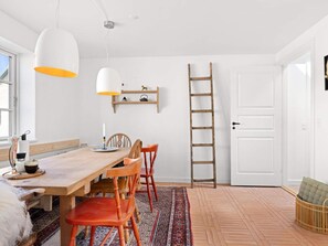 Un comedor con una mesa de madera, sillas rojas, una lámpara de techo blanca y una escalera apoyada en una puerta blanca.