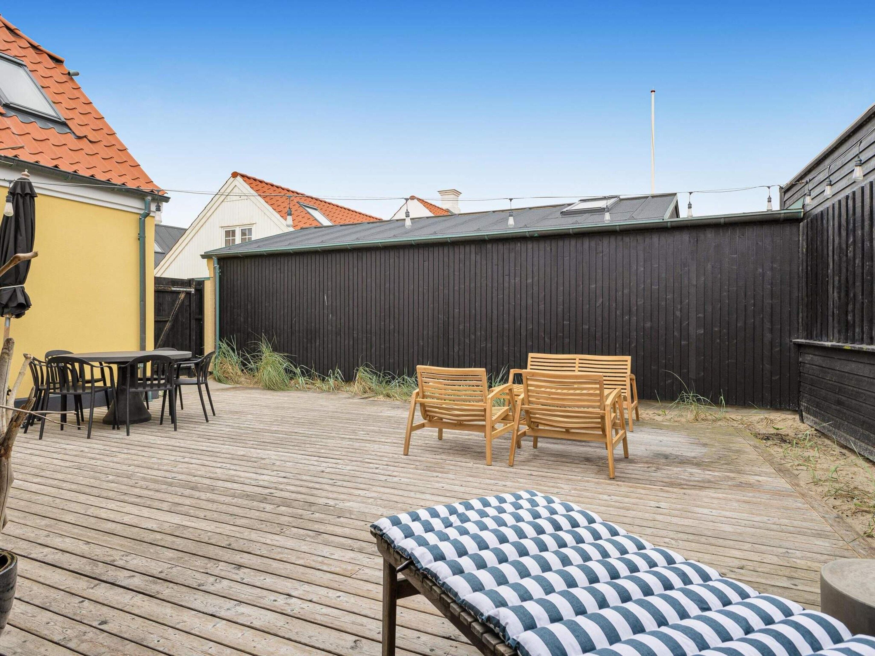 A wooden deck with a table and chairs, a bench, and a black fence in the background.