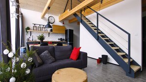 A modern living space with a dark grey sofa, a wooden coffee table, and a staircase with a blue railing. - Apartment Near Pernstejn Castle in Smrcek (Býšovec)