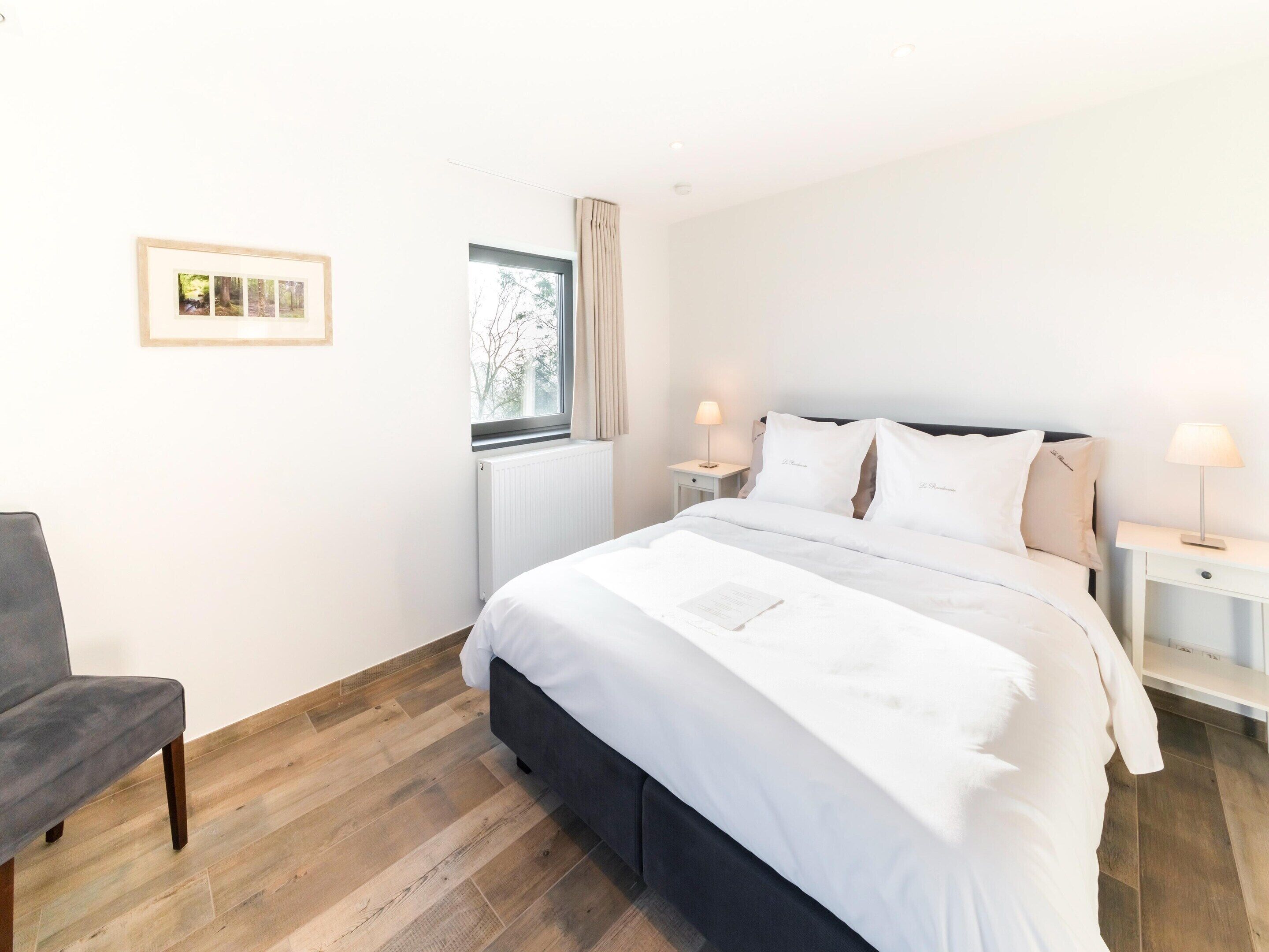 A neatly arranged bedroom with a bed, bedside tables, a chair, and a window.