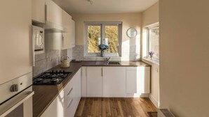 Une cuisine compacte avec des meubles blancs, une cuisinière à gaz, un four à micro-ondes et une fenêtre donnant sur des arbres.