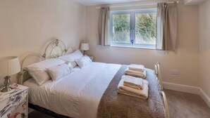 Un lit bien fait, avec du linge de lit blanc, une lampe de chevet et une table de chevet à motifs floraux.