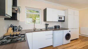 A modern kitchen with white cabinets, a microwave, a gas stove, and a washing machine. - Stunning Penthouse Apartment (Totland Bay)