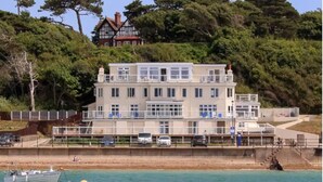A multi-story building with a balcony, located near a waterfront with a boat docked. - Stunning Penthouse Apartment (Totland Bay)