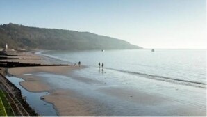 A beach with a calm sea, a few people walking, and a distant boat. - Stunning Penthouse Apartment (Totland Bay)