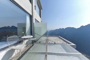 Een balkon met glazen hekwerk, een witte stoel, een kleine tafel en een vaas met een bloem.
