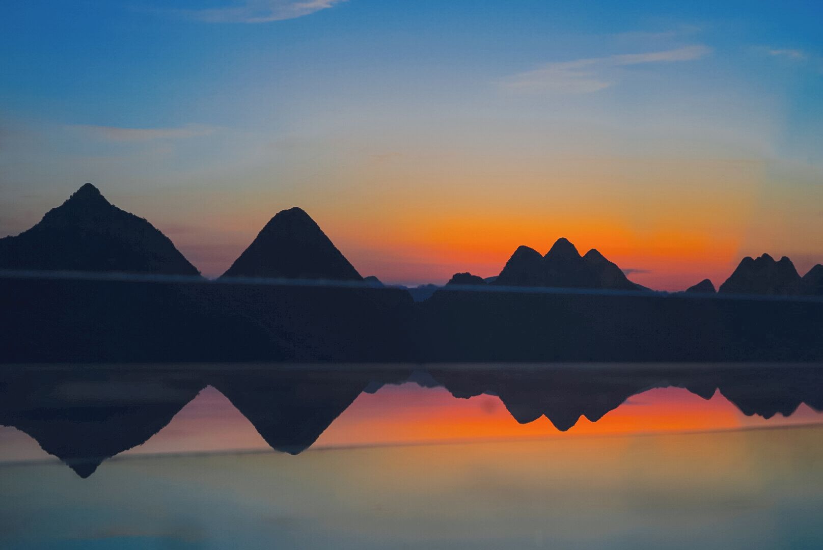 Un lac paisible où se reflètent les silhouettes des montagnes au coucher du soleil.
