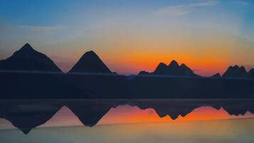 Un lac paisible où se reflètent les silhouettes des montagnes au coucher du soleil.