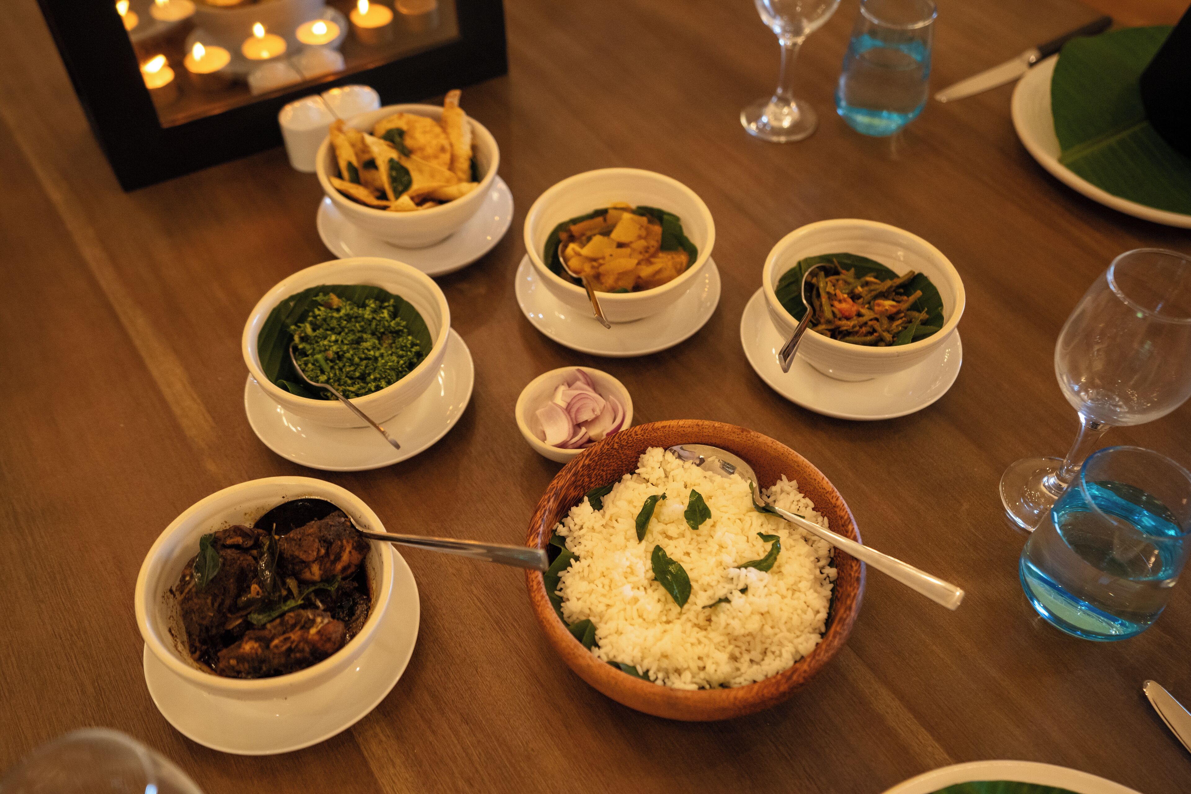 A table with various dishes, including rice, curry, and soup, along with glasses and cutlery.