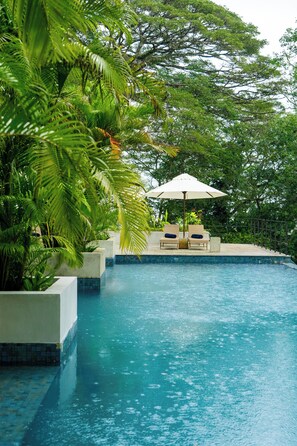 A swimming pool with a tiled edge, surrounded by lush greenery and a white umbrella. - Clodagh Manor House by Seven Angels (Rattota)