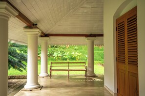 A covered porch with a wooden bench, white columns, and a wooden door. - Clodagh Manor House by Seven Angels (Rattota)