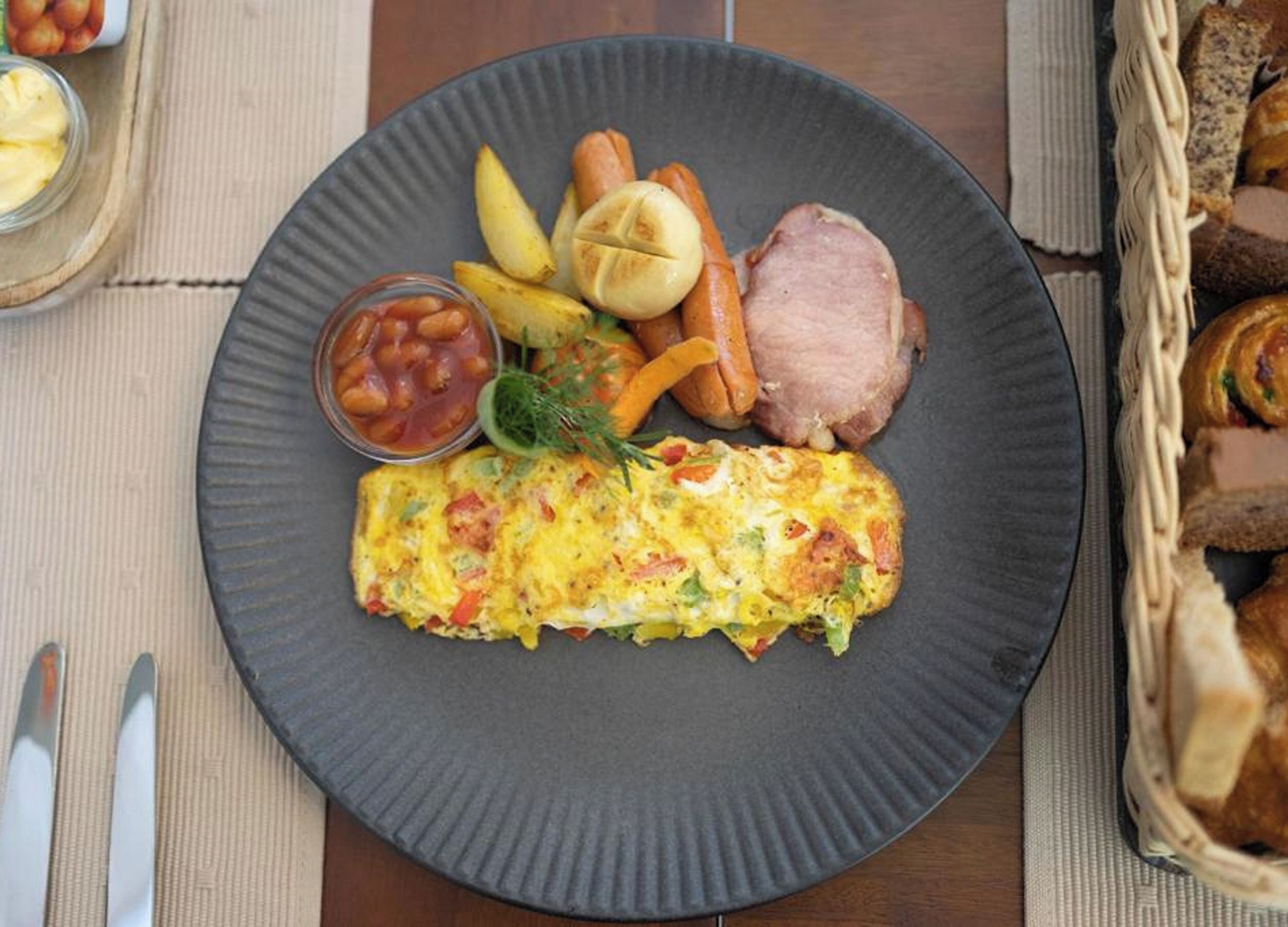 A plate with an omelette, roasted potatoes, carrots, and a slice of ham.