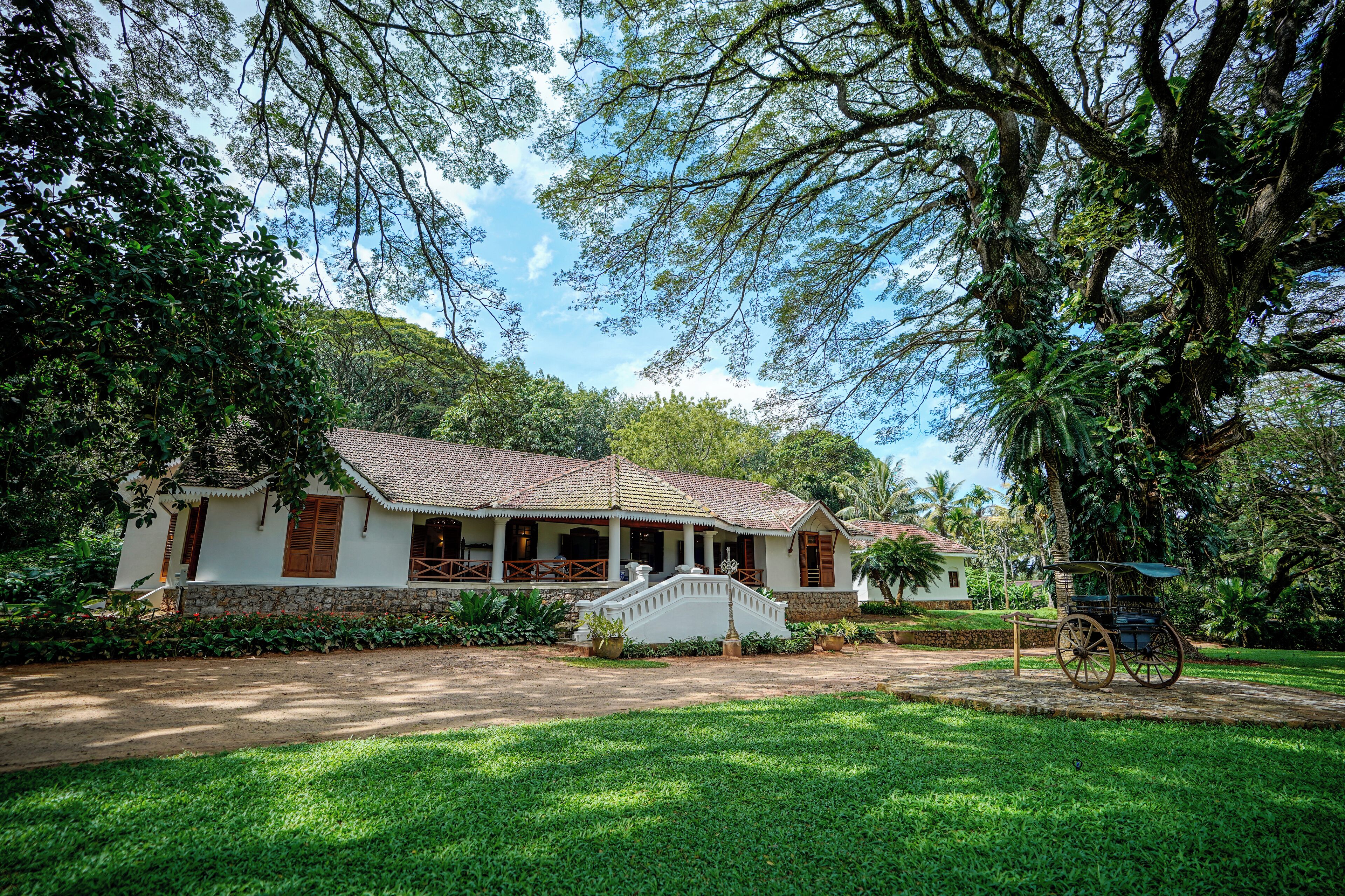 A traditional house with a porch, surrounded by lush greenery and a clear sky.