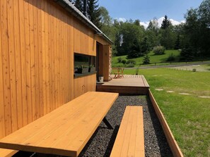 Ein Holzhaus mit einer Terrasse, Sitzmöglichkeiten im Freien und Blick auf eine grüne Landschaft.