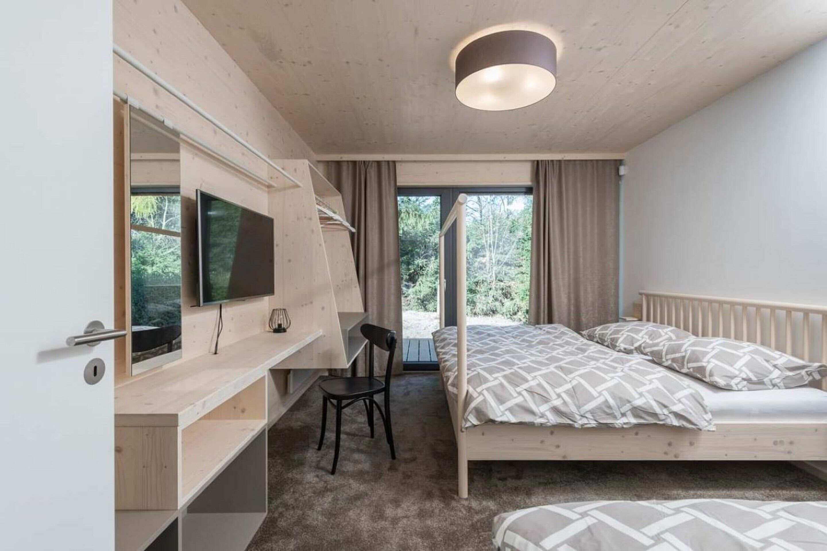 Une chambre à coucher avec un lit, un bureau et une chaise, une télévision et une fenêtre avec des rideaux.