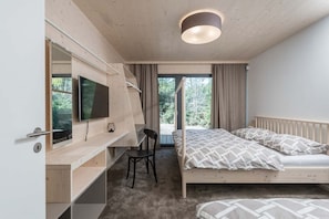 Ein Schlafzimmer mit einem Bett, einem Schreibtisch mit Stuhl, einem Fernseher und einem Fenster mit Vorhängen.