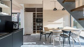 A modern kitchen with a built-in coffee machine, a dining area with a wooden table and chairs, and a large window providing natural light. - Villa in Bedrichov Near Ski Slopes (Bedrichov)
