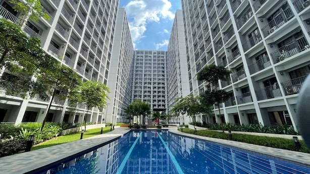 Un immeuble résidentiel moderne doté d’une piscine centrale, entouré de verdure et agrémenté de balcons en hauteur.