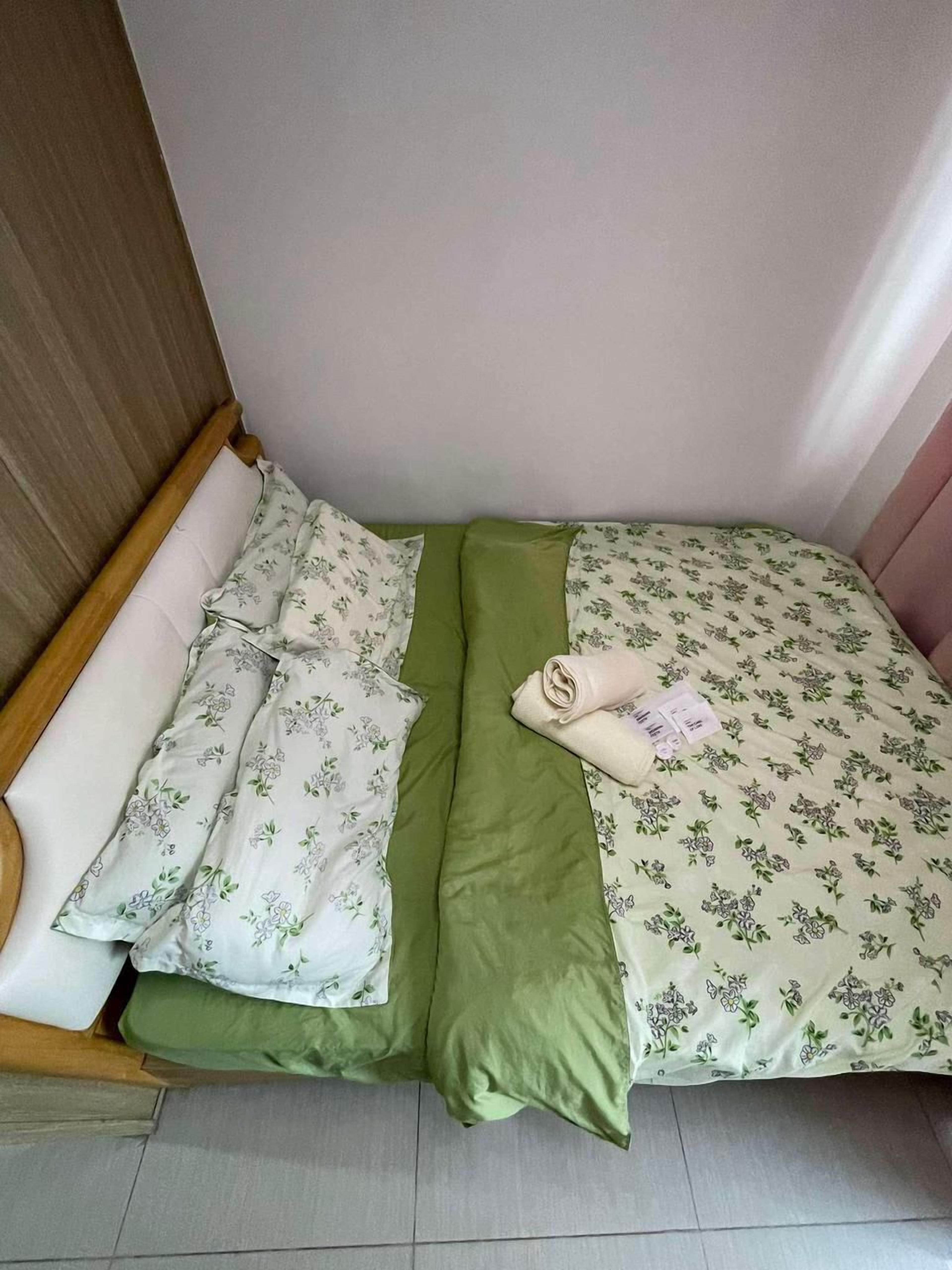 Un petit lit bien fait, avec une literie à motifs floraux, un oreiller vert et une serviette pliée.