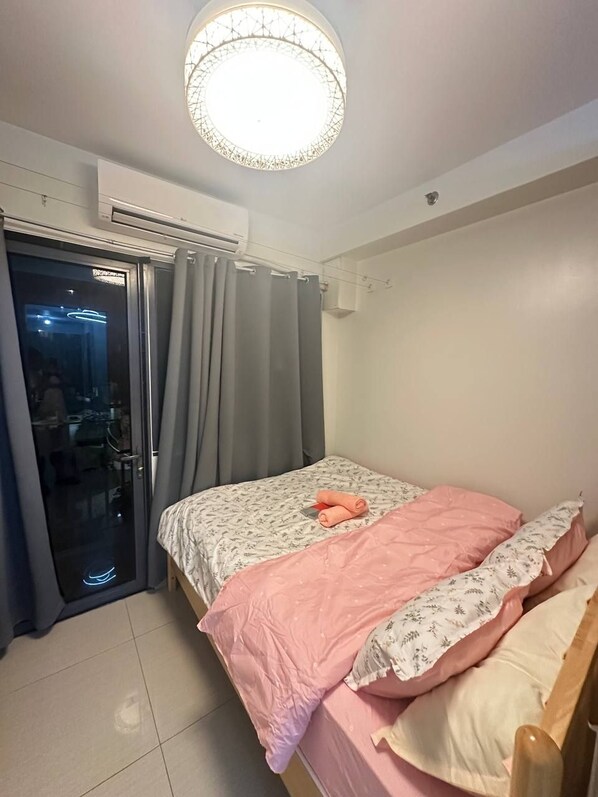 Un dormitorio con cama, lámpara de techo, unidad de aire acondicionado y puerta corrediza de vidrio que da a un balcón.