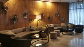 Un salon moderne avec un mur en bois aux lignes courbes, un canapé d’angle, une table basse ronde et un lampadaire.