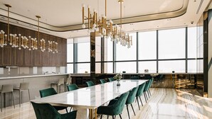 Ein moderner Essbereich mit einem langen Tisch, grünen Stühlen und einer Chandelüster.