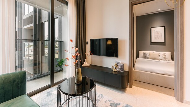Ein modernes Schlafzimmer mit einem großen Bett, einem Fernseher und einer Glastür, die auf einen Balkon führt.