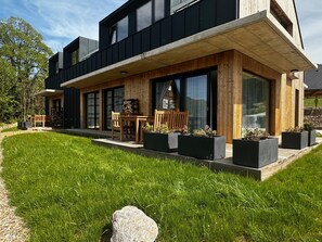 Een modern herenhuis met twee verdiepingen, een overdekt terras, grote ramen en een verzorgd gazon.