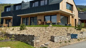 Ein modernes, zweistöckiges Haus mit Steinfundament, großen Fenstern und einer Holzterrasse.