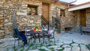 A stone building with a patio area featuring a round table with chairs, a wooden door, and a small window with a potted plant. - romantic house for 2 people with jacuzzi (Laroya)