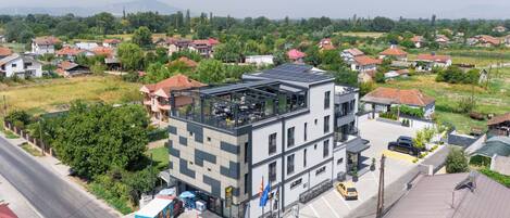 A multi-story building with a rooftop terrace, surrounded by residential houses and greenery.