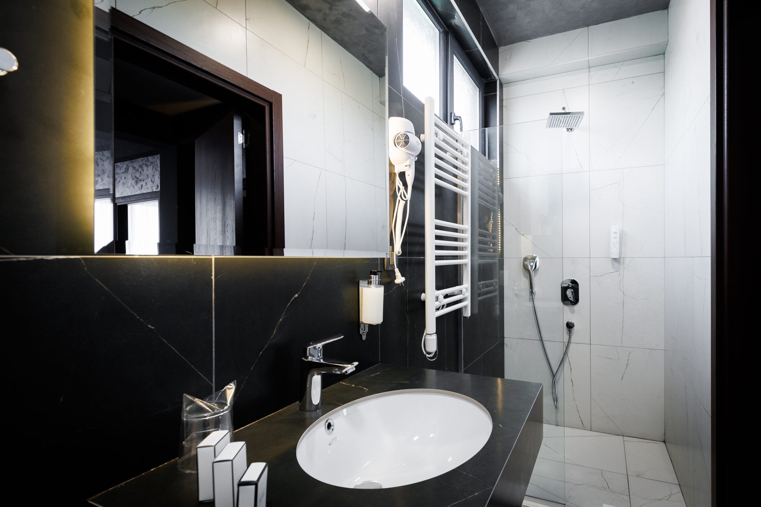 A modern bathroom with a large mirror, a sink, a towel rack, and a shower area.